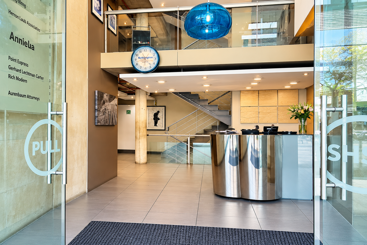 Modern office building entrance featuring a sleek reception desk, glass doors, and a prominent staircase leading to the upper level.