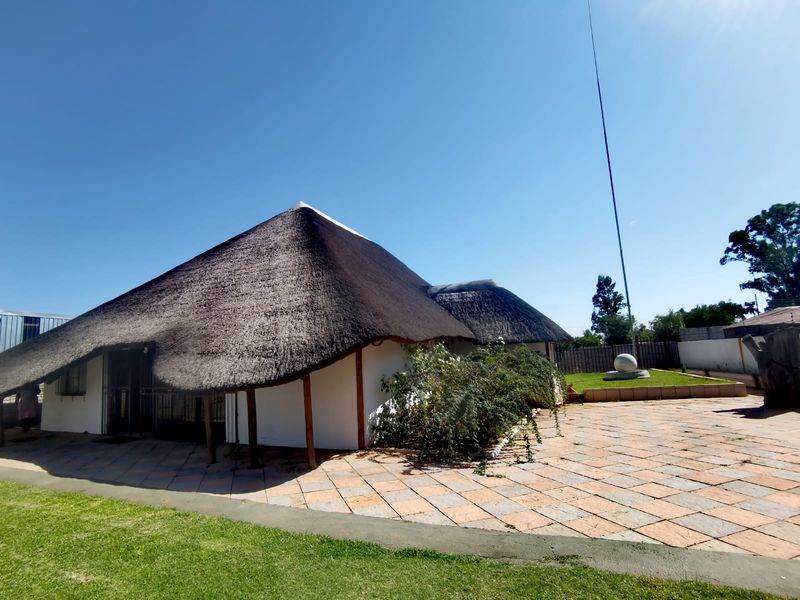 Rear view of a traditional thatched-roof farmhouse featuring a large tiled patio area and surrounding garden space.