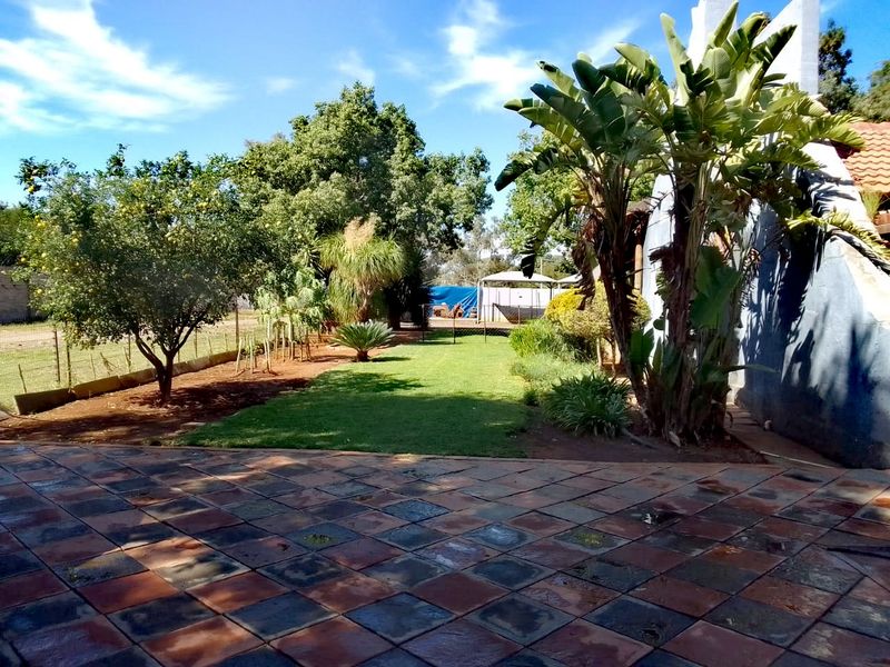 A well-maintained garden area featuring a tiled patio, lush lawn, and mature trees, providing a pleasant outdoor space for the farm property.