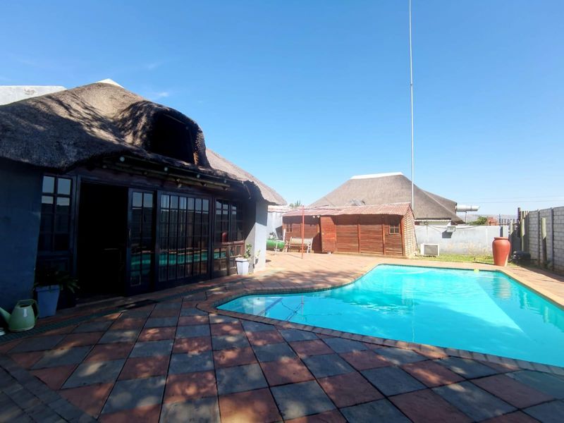 Outdoor pool area featuring a paved patio, swimming pool, and a structure with a traditional thatched roof and timber-framed glass doors.