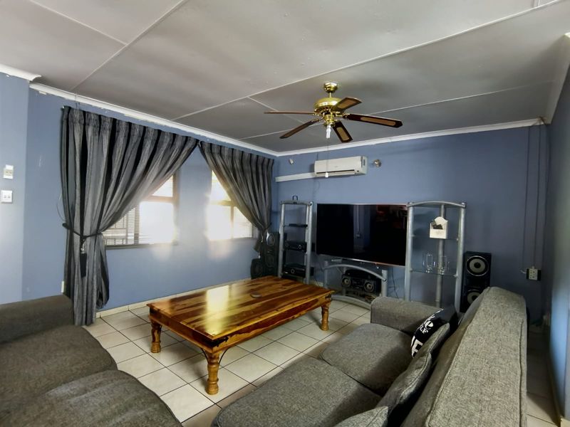 A comfortable living room featuring tiled flooring, a ceiling fan, and a wall-mounted split-system air conditioner.
