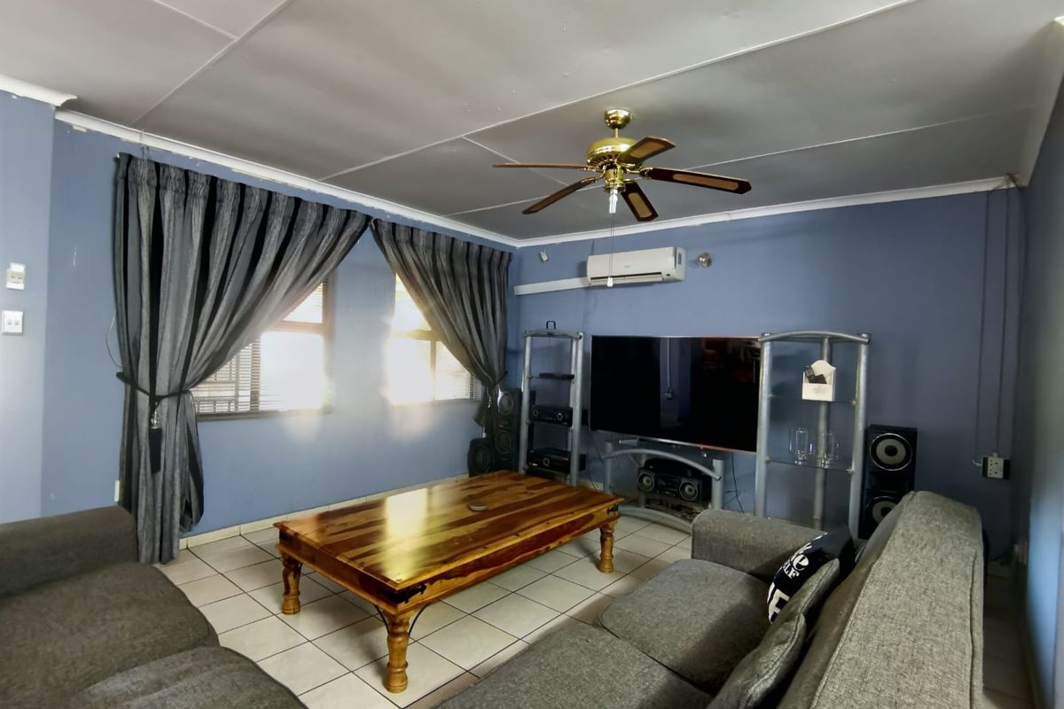 A comfortable living room featuring tiled flooring, a ceiling fan, and a wall-mounted split-system air conditioner.