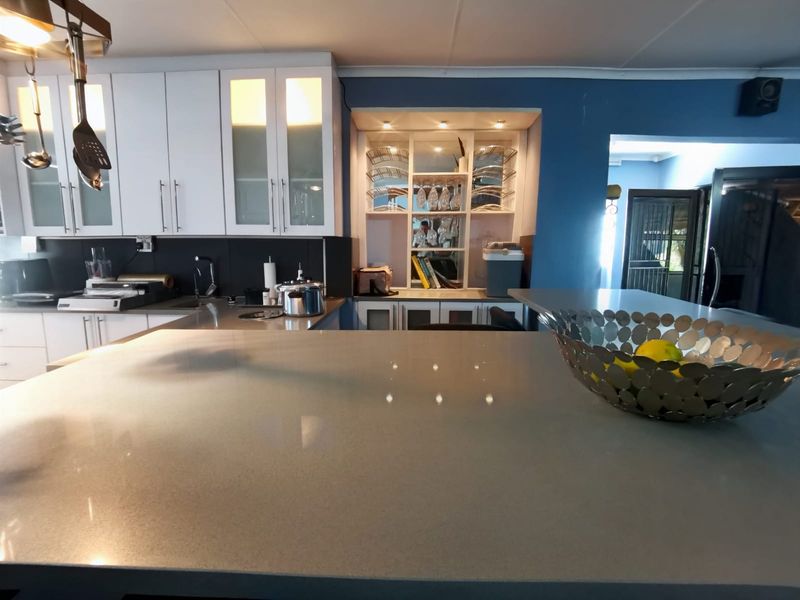 Modern kitchen featuring a large island with quartz countertops, white cabinetry, glass-front display units, and integrated lighting.