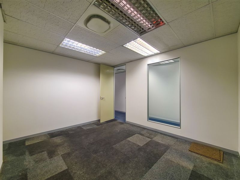 A clean, empty office space featuring carpet tiles, a suspended ceiling with recessed lighting, and an internal glass partition for natural light.