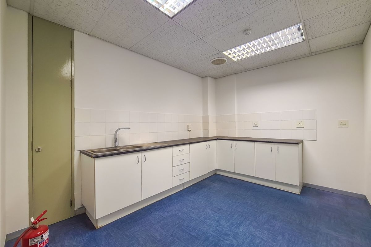 A functional office kitchenette featuring white cabinetry, laminate countertops, a stainless steel sink, and durable vinyl flooring.