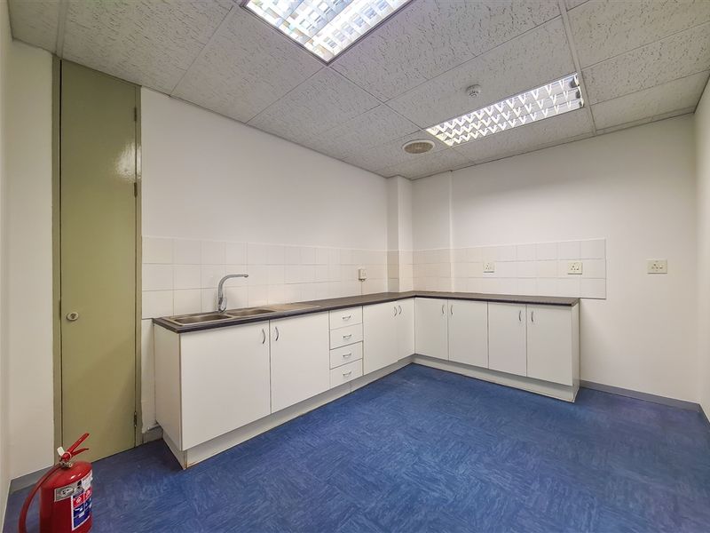 A functional office kitchenette featuring white cabinetry, laminate countertops, a stainless steel sink, and durable vinyl flooring.