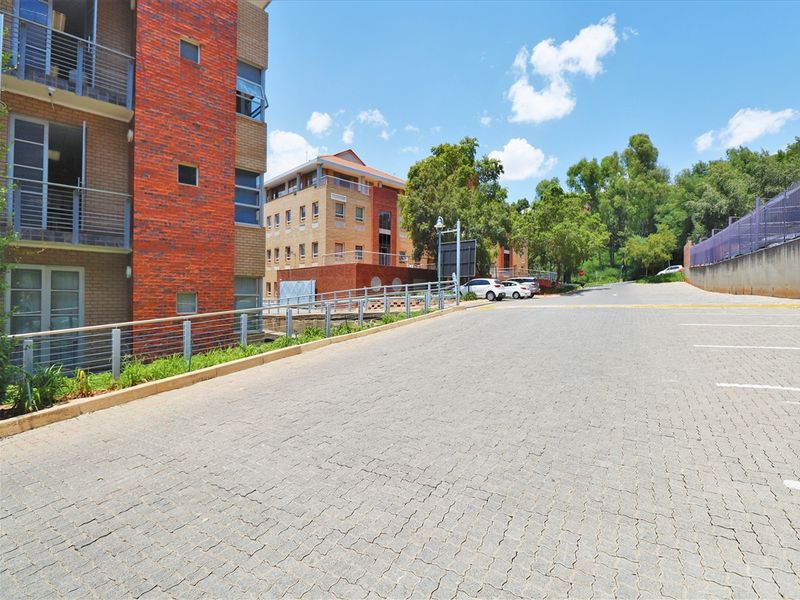 Exterior view of a multi-story office building featuring brick facade, paved driveway, and designated parking areas.