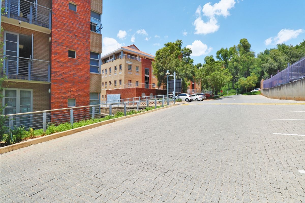 Exterior view of a multi-story office building featuring brick facade, paved driveway, and designated parking areas.