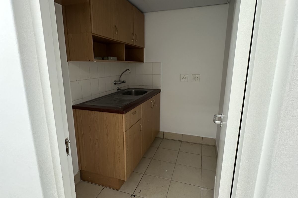 A small office kitchenette featuring wooden cabinetry, a stainless steel sink, and tiled flooring, requiring minor maintenance and cosmetic updates.