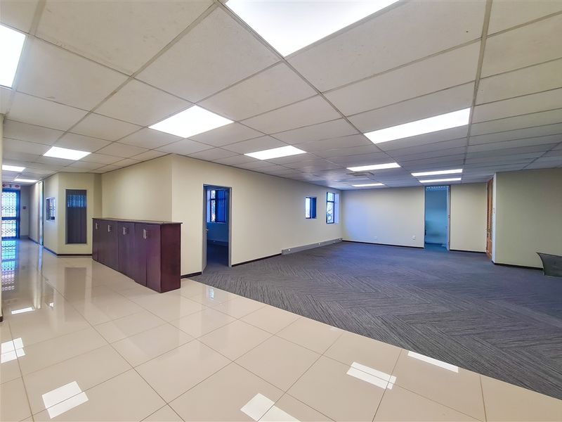 Spacious open-plan office area featuring a mix of tiled and carpeted flooring, suspended ceilings with recessed lighting, and built-in storage cabinetry.