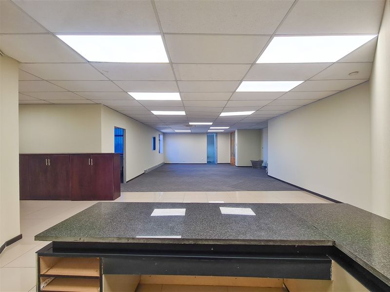 An open-plan office space featuring a mix of tiled and carpeted flooring, recessed lighting, and built-in cabinetry with some missing doors.