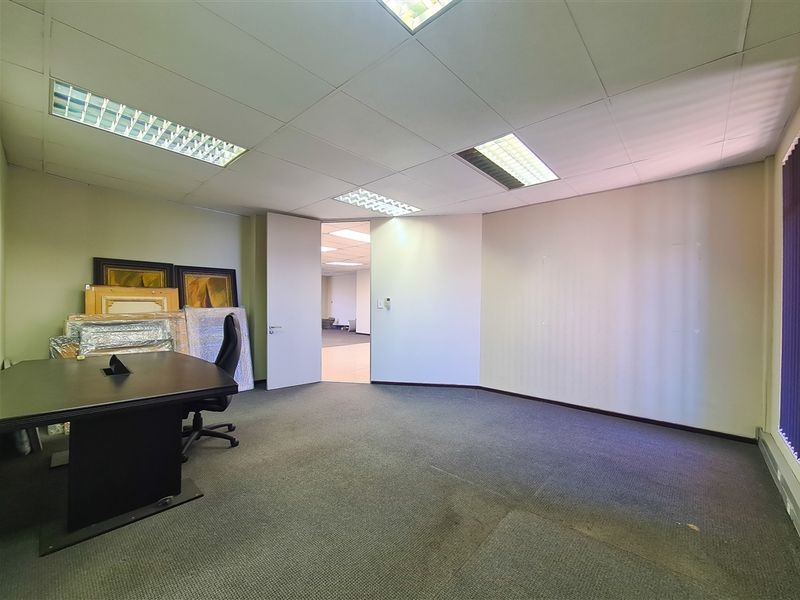 A functional office space featuring a suspended ceiling with recessed lighting, carpeted flooring, and an open doorway leading to an adjacent area.