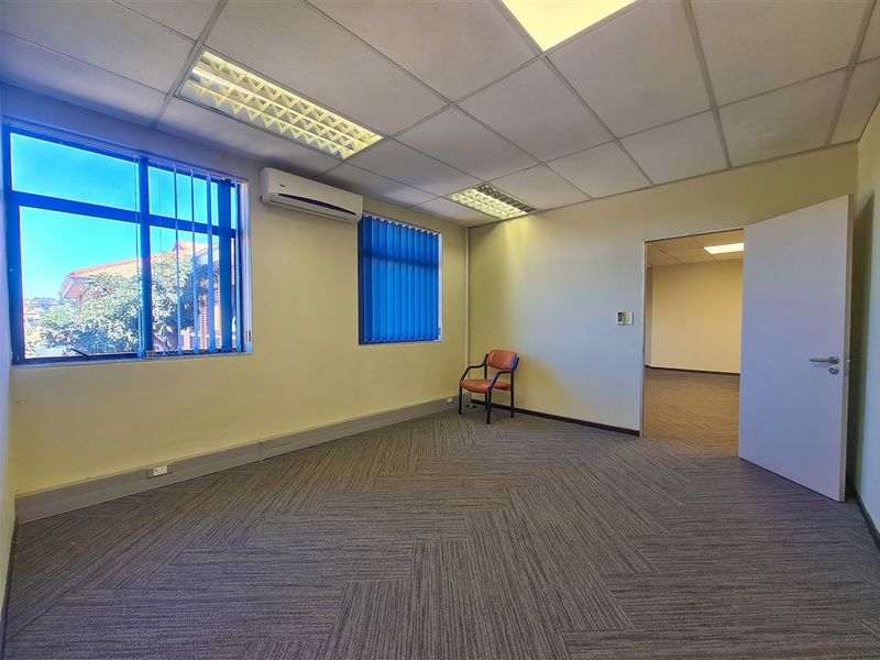 A vacant office space featuring carpet tiles, a suspended ceiling with recessed lighting, and a wall-mounted air conditioning unit.