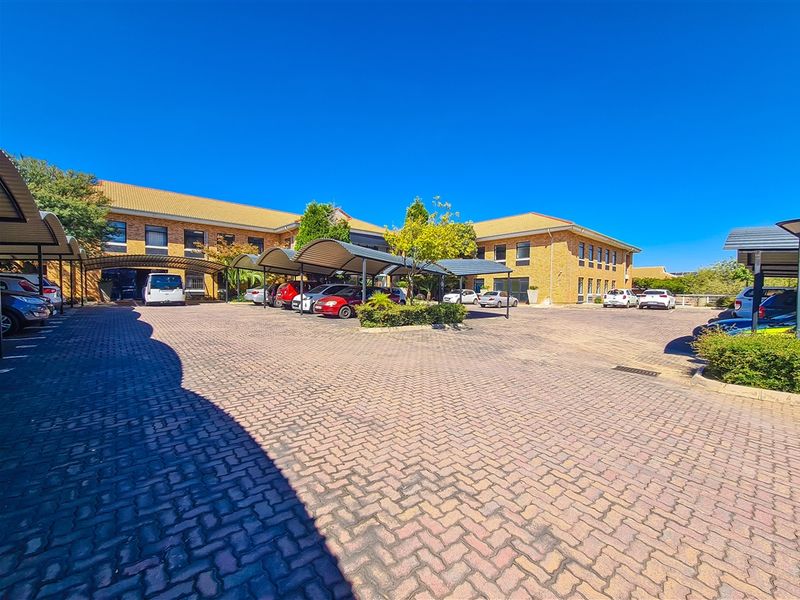 Exterior view of the office building featuring a large paved parking area with multiple covered carport structures and brick facade.