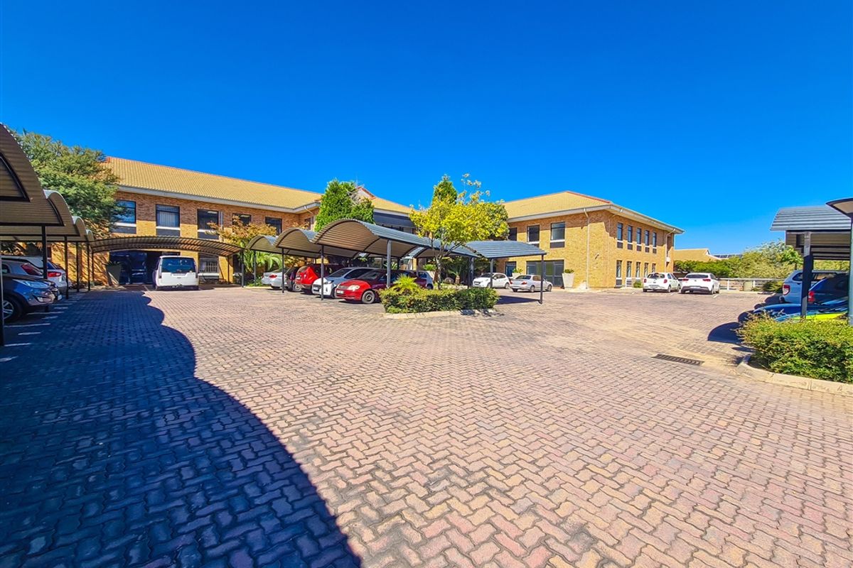Exterior view of the office building featuring a large paved parking area with multiple covered carport structures and brick facade.