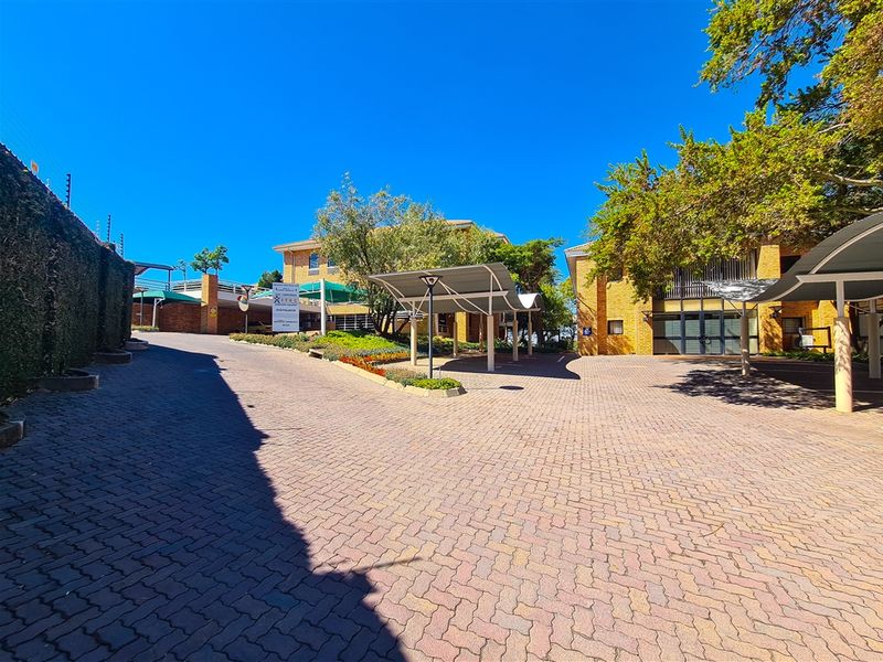 A well-maintained office complex exterior featuring a paved driveway, covered parking bays, and established landscaping with brick building facades.