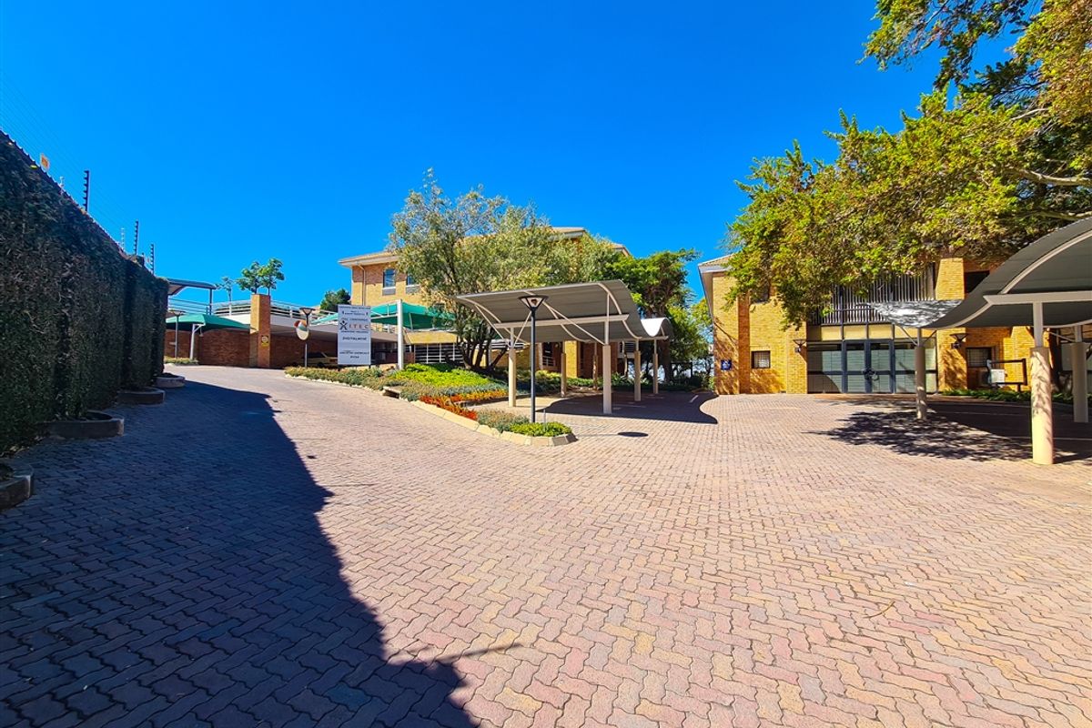 A well-maintained office complex exterior featuring a paved driveway, covered parking bays, and established landscaping with brick building facades.