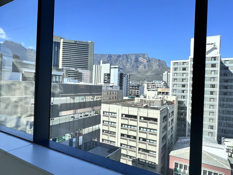 A clear, elevated city view looking out from an office window towards the mountain skyline.