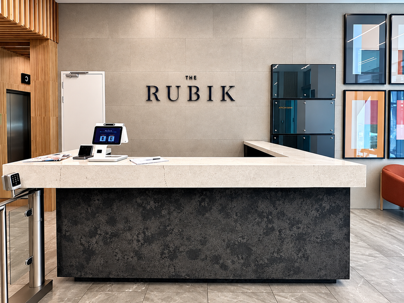 Modern office building lobby featuring a professional reception desk, stone finishes, integrated security turnstiles, and high-end architectural lighting.