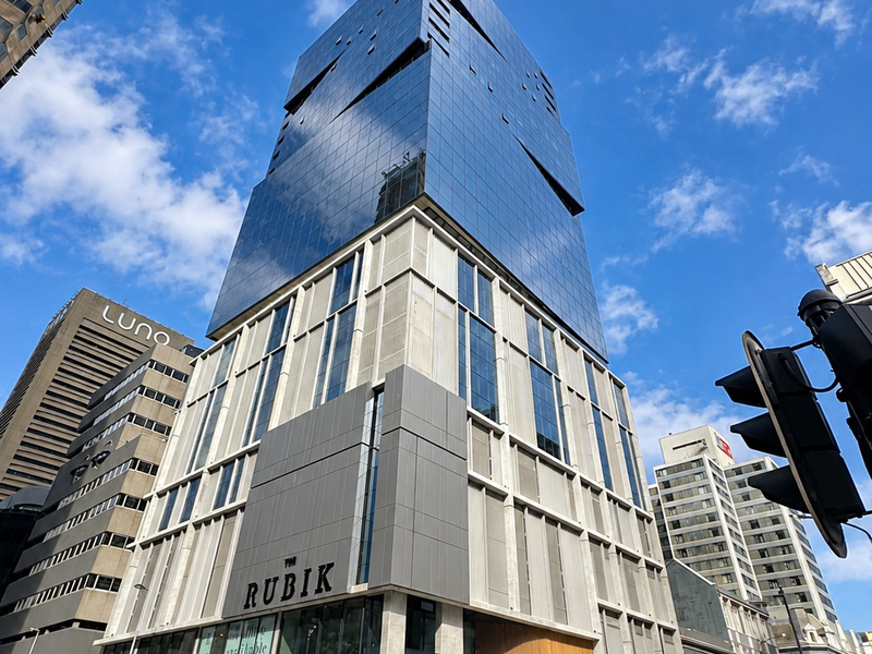 Modern high-rise office building featuring a striking glass facade and concrete structural design, located in a prominent urban street corner setting.