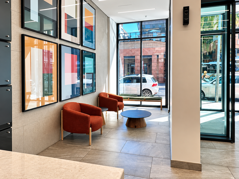 Modern office entrance lobby featuring large format floor tiles, recessed linear lighting, and a floor-to-ceiling glass facade with street views.