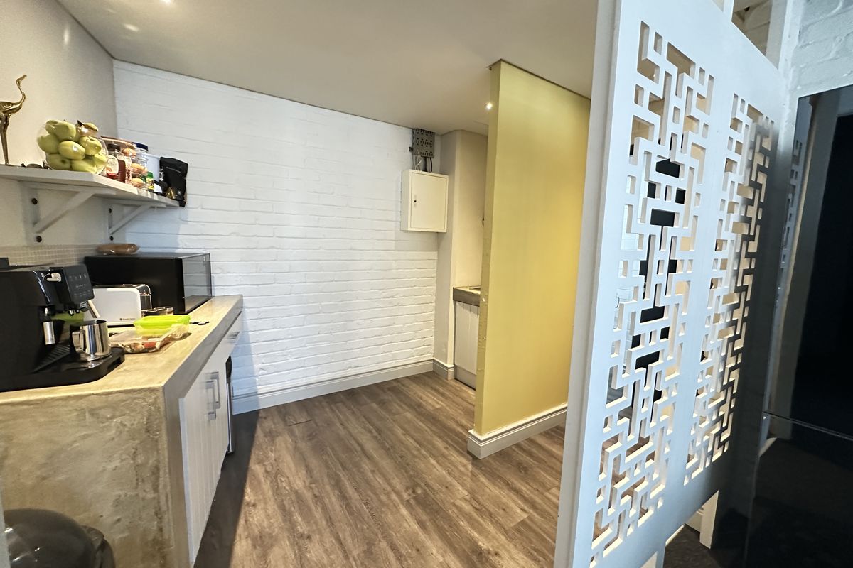 A compact office kitchenette area featuring a built-in counter, sink, and decorative partition screen, finished with wood-look flooring and painted brick walls.
