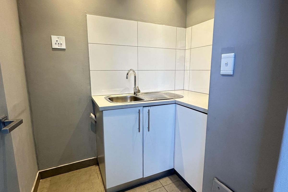 A compact kitchenette area featuring built-in cabinetry, a stainless steel sink, and tiled splashback, suitable for office use.