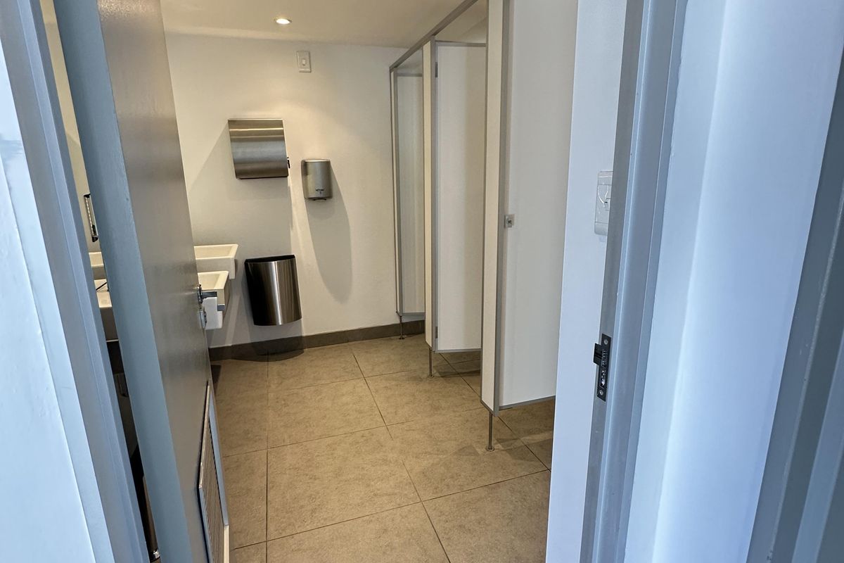 A clean, functional office restroom featuring tiled flooring, multiple toilet cubicles, and wall-mounted stainless steel hand hygiene dispensers.