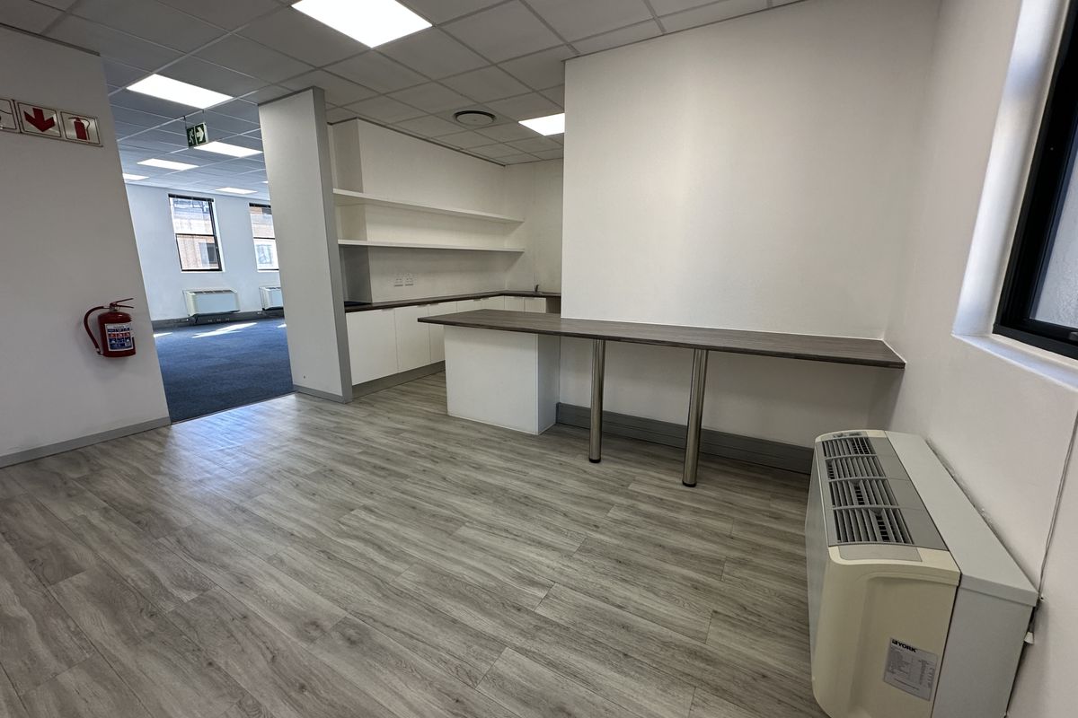 A clean, modern office kitchenette area featuring built-in cabinetry, open shelving, a breakfast bar, and wood-look laminate flooring.
