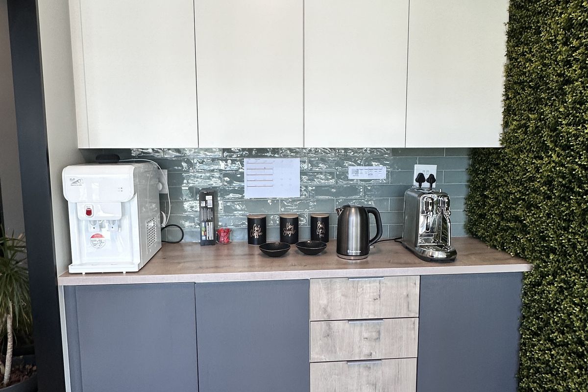 A modern office kitchenette featuring sleek two-tone cabinetry, a textured backsplash, and wood-look flooring, providing a functional break area.