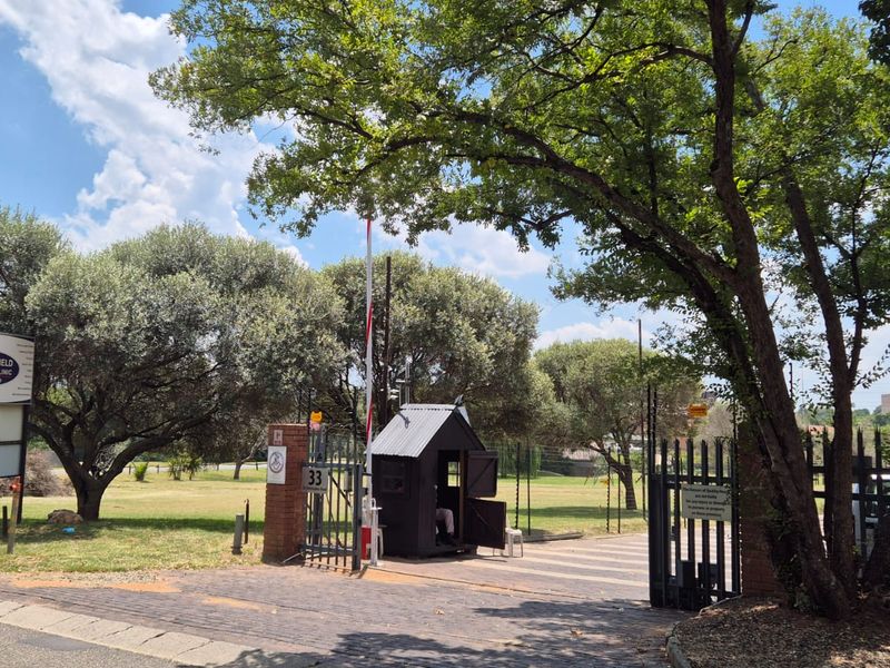 Entrance to the office property featuring a paved driveway, security boom gate, and a dedicated guard booth.
