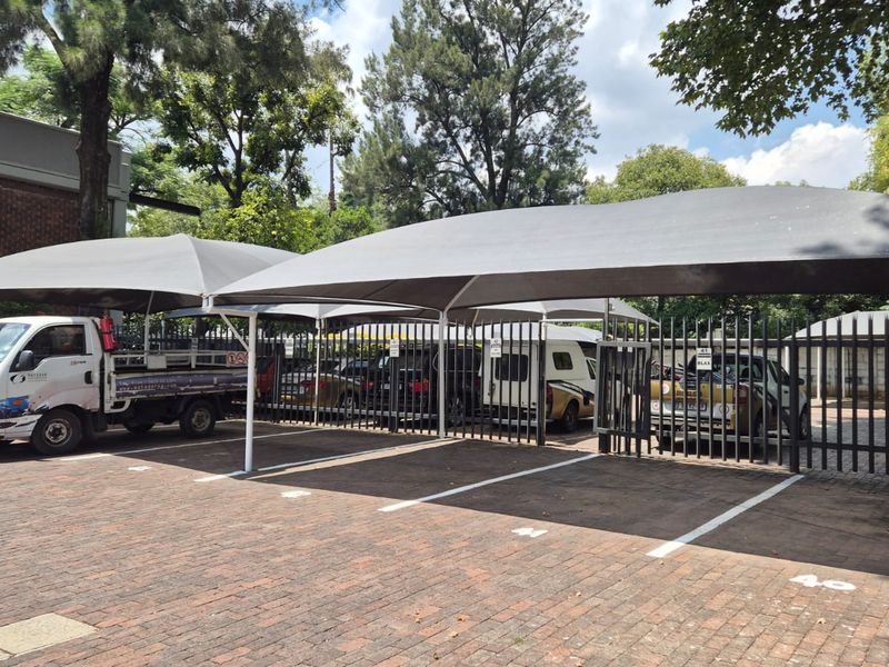 Outdoor parking area featuring multiple shade cloth carports, paved surfacing, and secure steel perimeter fencing.
