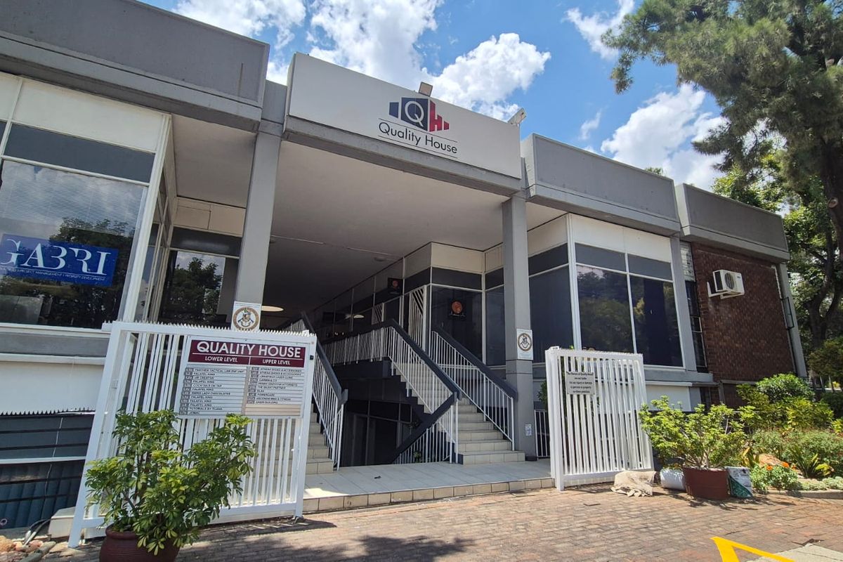 Front elevation of Quality House office building featuring a paved entrance, external signage, metal security gates, and a central staircase leading to the upper level.