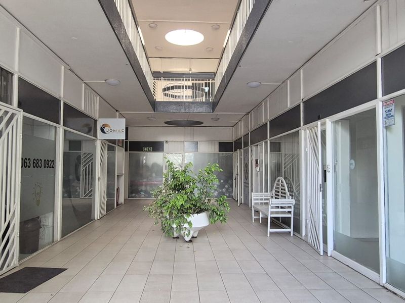 A bright, open-plan office building hallway featuring glass-fronted units, tiled flooring, and a central atrium design, providing a professional and accessible commercial environment.