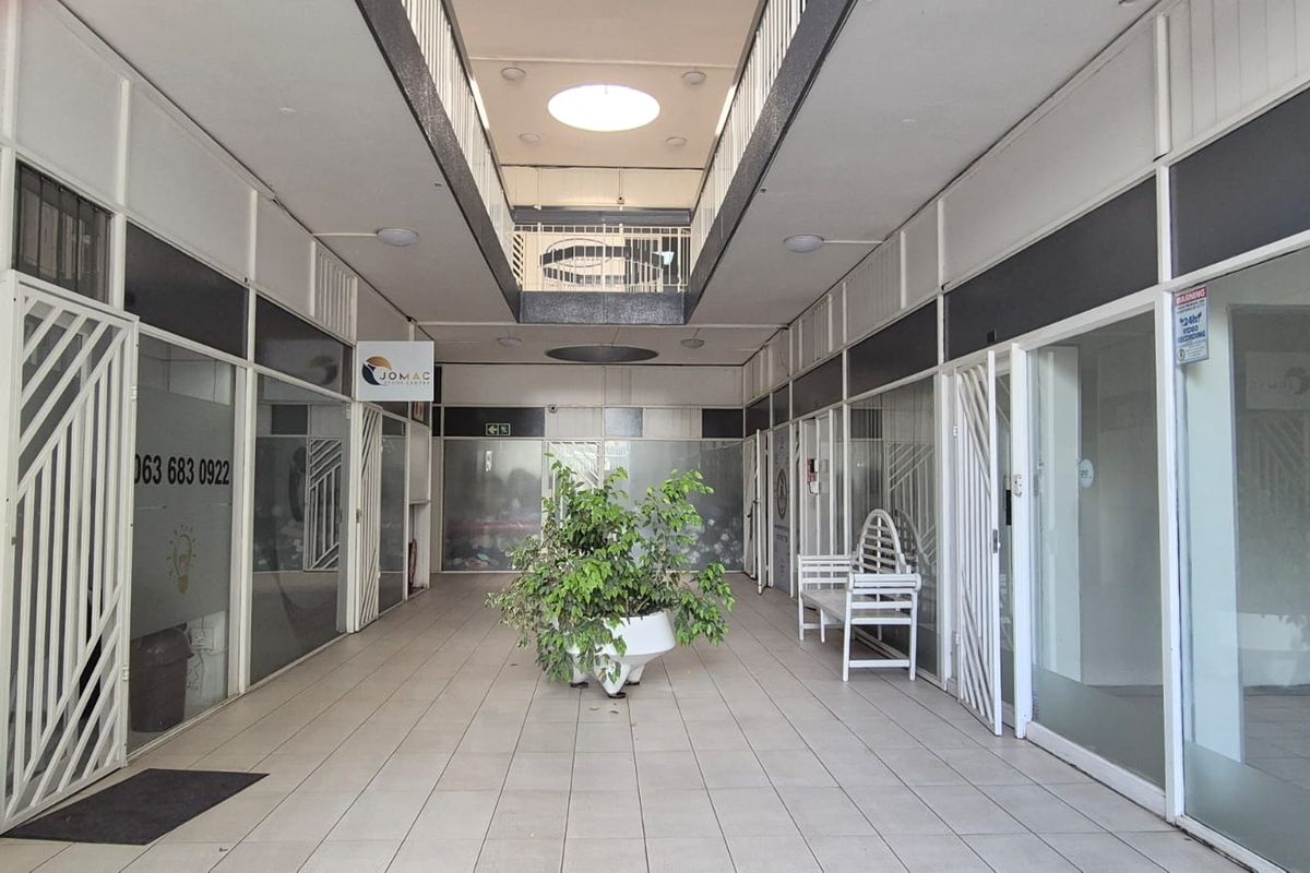 A bright, open-plan office building hallway featuring glass-fronted units, tiled flooring, and a central atrium design, providing a professional and accessible commercial environment.