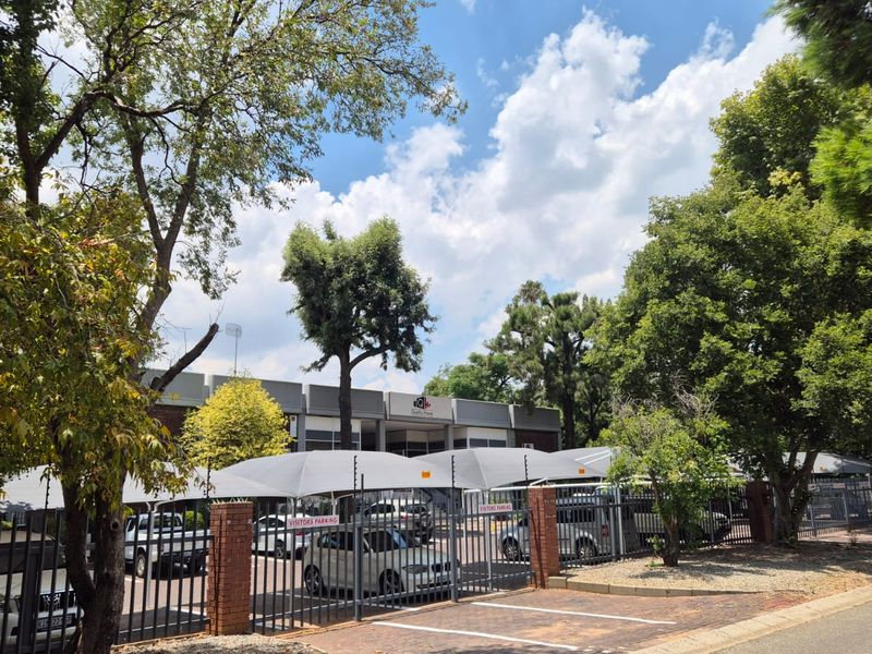 Front exterior view of the office property featuring a paved parking area with shade cloth carports, secured by brick walls and metal fencing.