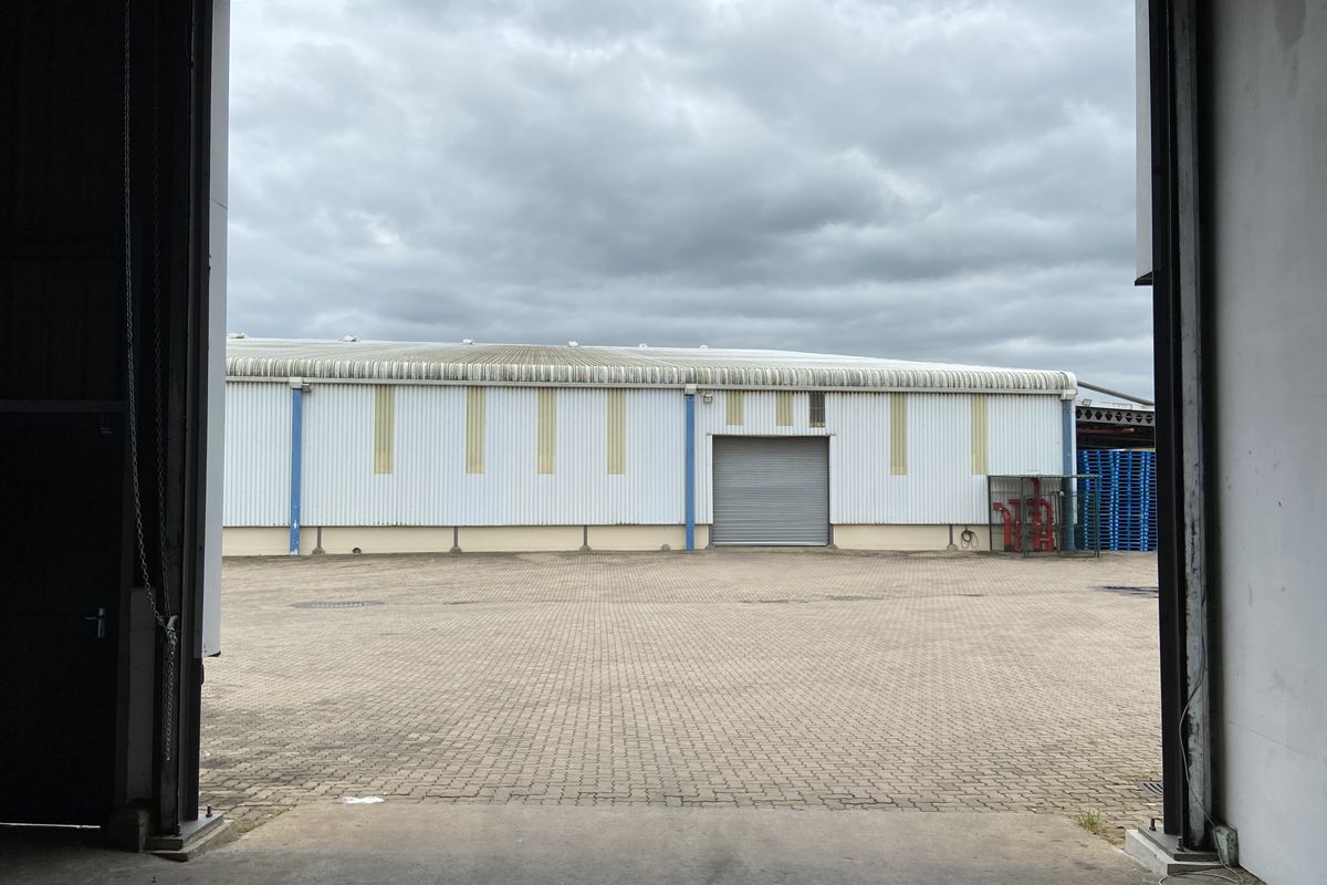 View of an industrial yard and rear building facade featuring corrugated metal cladding, a roller shutter door, and paved exterior space.