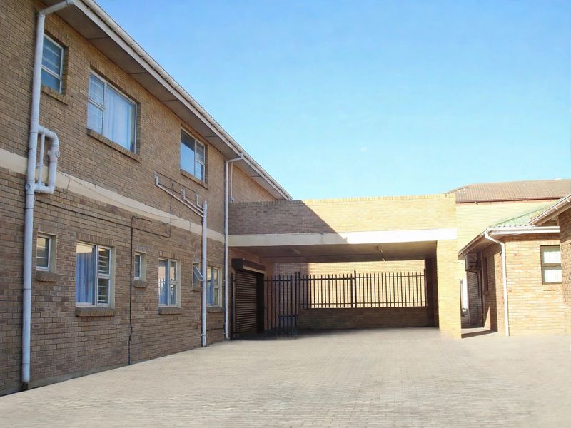 A view of the rear exterior area featuring a face brick building, paved driveway, and a covered carport with security gate access.