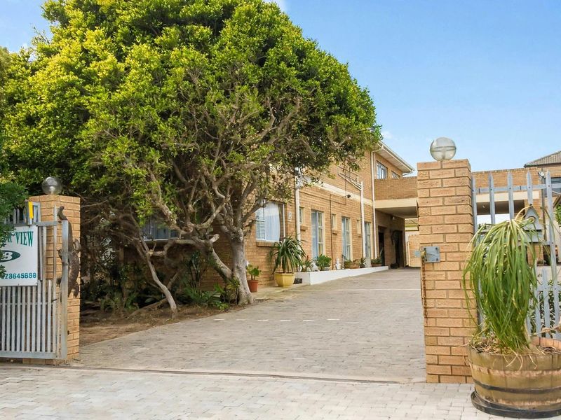 Front entrance view of the guest house featuring a paved driveway, brick boundary walls, and secure metal gate access.