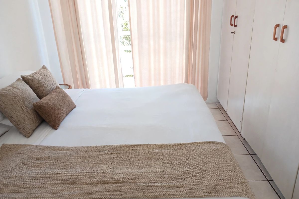 A bedroom featuring built-in cupboards, tiled flooring, and a sliding glass door providing natural light.