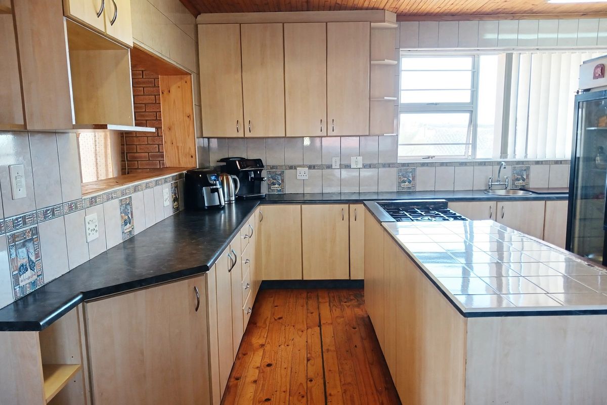 A functional kitchen featuring light-toned cabinetry, a tiled island with a built-in gas hob, timber flooring, and a timber-clad ceiling.