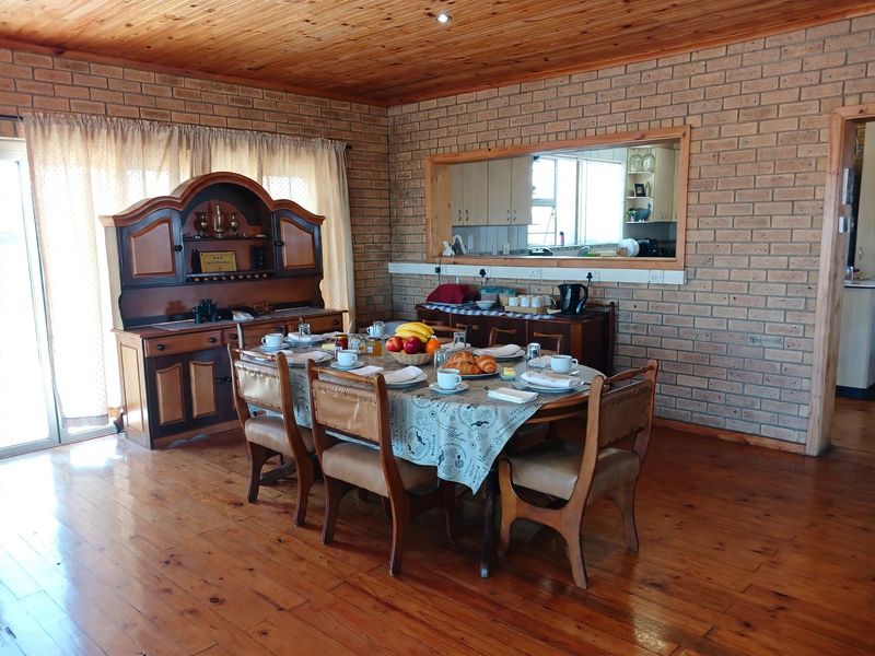 Dining room featuring exposed brick walls, timber ceiling, and hardwood flooring, with a convenient serving hatch connecting to the kitchen area.