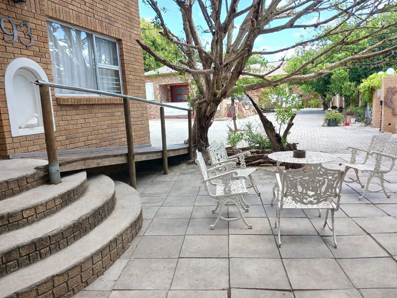 Front exterior area featuring a brick facade, curved concrete steps with a metal handrail, a wooden ramp, and a paved patio seating area.