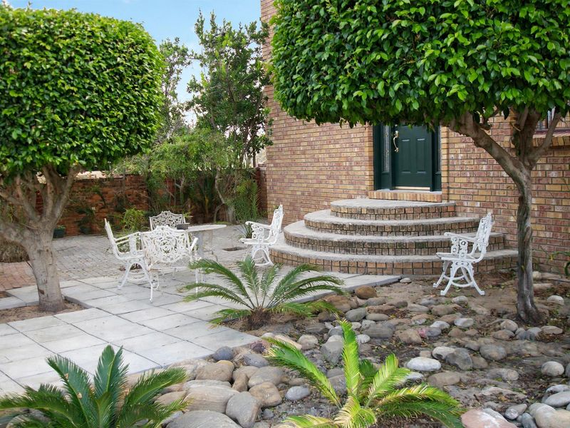 A well-maintained rear garden area featuring a paved patio, brick steps leading to the entrance, and established landscaping.