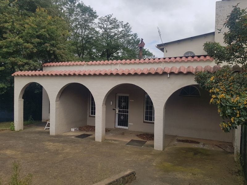Rear exterior view featuring a covered patio with arched masonry columns, terracotta roof tiles, and concrete paving.