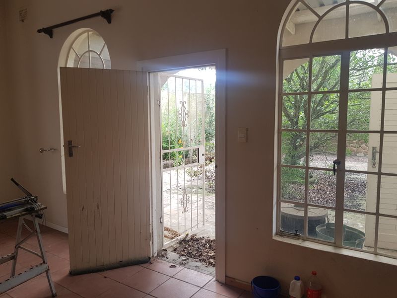 An empty living area featuring arched windows, tiled flooring, and direct access to an outdoor patio through a security gate and timber door.