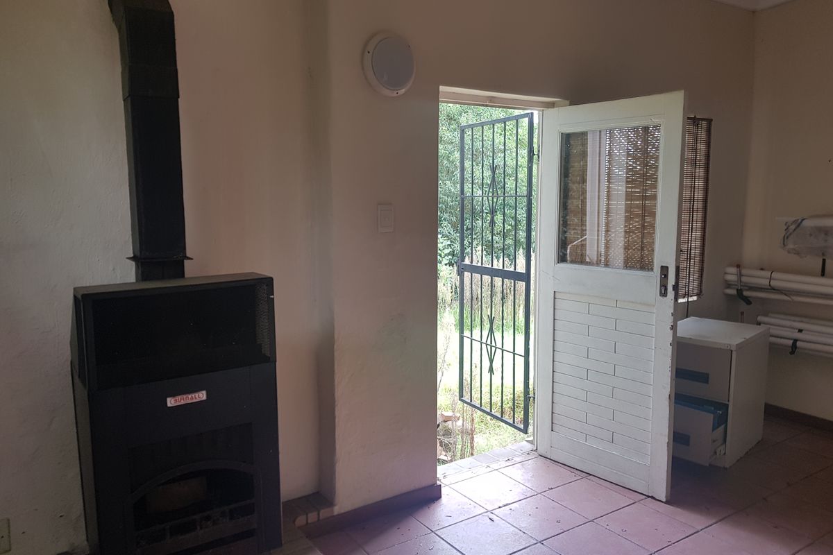 An empty living area featuring a black freestanding fireplace, tiled flooring, and direct access to the exterior through a security gate and door.