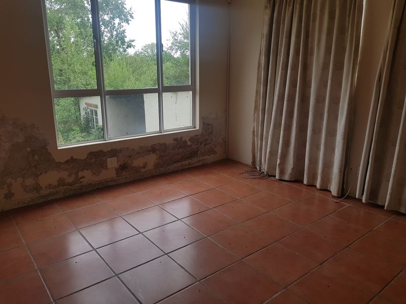 Empty office space featuring tiled flooring and a large window, currently showing significant wall damage and damp staining requiring repair.