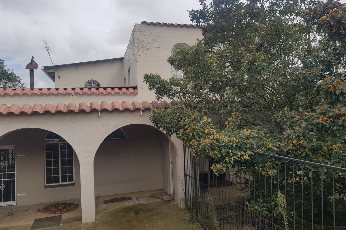 Rear exterior view of a commercial building featuring a covered arched patio, terracotta roof tiles, and mature landscaping.