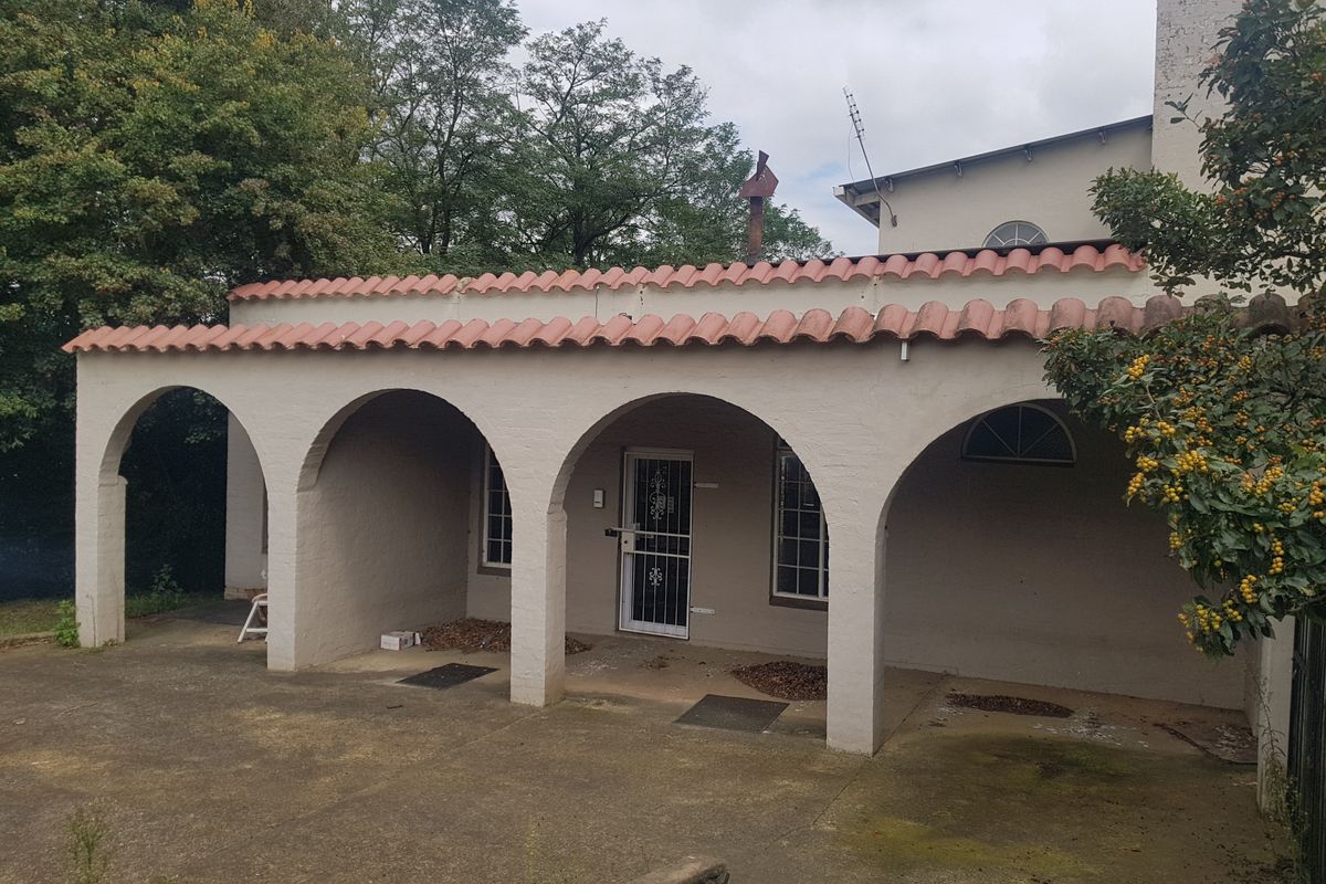 Rear exterior view featuring a covered patio with arched masonry columns, terracotta roof tiles, and concrete paving.